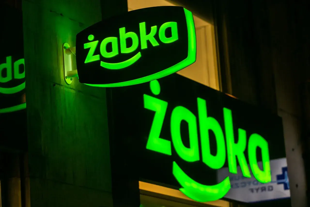 Dwa zielone, podświetlane neony z logo "Żabka" na ciemnej ścianie.